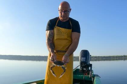 Un pescador sostiene un cangrejo azul en la laguna de Orbetello, Italia, el lunes 14 de agosto de 2023. (AP Foto/Luigi Navarra)