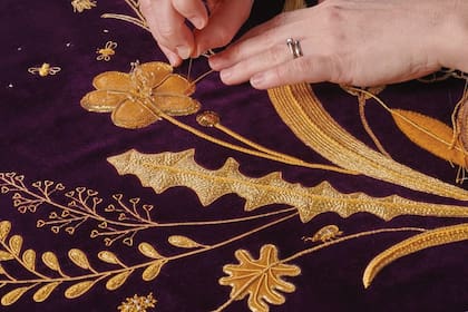 Un plano detalle de la "robe" la Reina usará a la salida de la Abadía. Se trata de una prenda nueva, realizada por Ede y Ravenscroft y bordada a mano por la Royal School of Needlework, de la cual Camilla es patrona desde 2017. Es de terciopelo púrpura (un color que combina con la que el Rey usará en la salida), tiene los emblemas del Reino Unido y rinde homenaje al Rey y, además, elementos vinculados con la naturaleza.