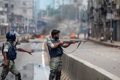 Un policía apunta su arma hacia un grupo de manifestantes durante un toque de queda impuesto en medio de violentas protestas contra la primera ministra Sheikh Hasina y su gobierno, en Daca, Bangladesh, el lunes 5 de agosto de 2024
