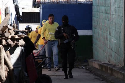 Un policía de fuerzas especiales vigila a presos que se dirigen a pintar encima de los grafitos hechos por pandilleros en paredes en la comunidad Las Brisas, en Soyapango, el Salvador, el lunes 14 de noviembre de 2022. (AP Foto/Salvador Melendez)