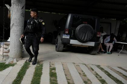 Un policía guatemalteco camina cerca de presuntos traficantes de migrantes, a la derecha, quienes fueron detenidos durante una operación contra una supuesta red de "coyotes" en Huehuetenango, Guatemala, cerca de la frontera con México, el martes 2 de agosto de 2022.  (AP Foto/Moisés Castillo)