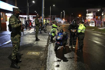 Un policía pide identificación a un motociclista mientras soldados montan guardia, en Bogotá