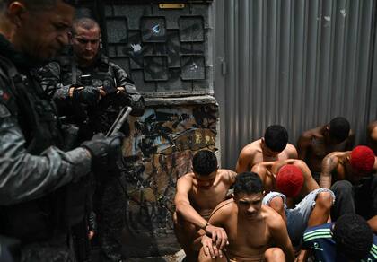 Un policía revisa su teléfono móvil junto a sospechosos arrestados durante la Operación Contención en la favela Vila Cruzeiro, en el complejo Penha, Río de Janeiro