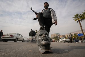 Un rebelde sirio sobre un busto de fallecido presidente sirio Hafez Assad en Damasco el 8 de diciembre del 2024. (AP foto/Hussein Malla)
