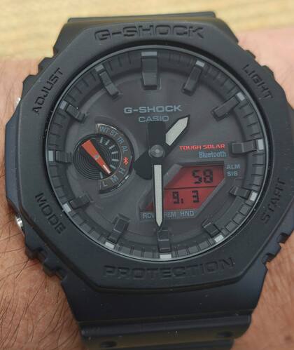 Un reloj Casio GA-B2100BBR-1A con cuadrante analógico, panel solar, conexión Bluetooth, y una pequeña pantalla LCD de fondo rojo