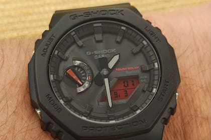 Un reloj Casio GA-B2100BBR-1A con cuadrante analógico, panel solar, conexión Bluetooth, y una pequeña pantalla LCD de fondo rojo