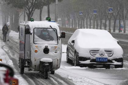 Un repartidor pasa junto a un auto cubierto de nieve recién caída en Beijing, China, el domingo 7 de noviembre de 2021. Una tormenta al principio de la temporada cubrió de nieve buena parte del norte de China, incluida la capital, Beijing, y provocó cortes de carreteras y cancelaciones de vuelos. (AP Foto/Ng Han Guan)