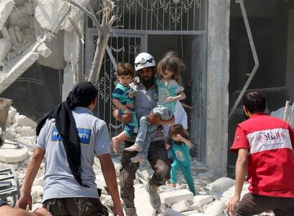 Un rescatista salva a chicos sirios tras un ataque con bombas barril ayer, en Aleppo