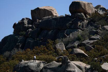 Un solicitante de asilo intenta hallar señal para su teléfono celular ascendiendo por unas rocas tras cruzar la frontera desde México, el miércoles 20 de septiembre de 2023, cerca de Jacumba Hot Springs, California. (AP Foto/Gregory Bull)