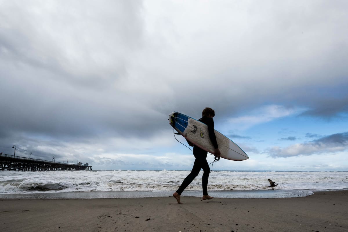 Un surfista se encamina hacia el agua mientras una tormenta se desplaza por el área (AP, archivo)