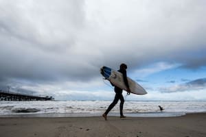 Un surfista se encamina hacia el agua mientras una tormenta se desplaza por el área (AP, archivo)