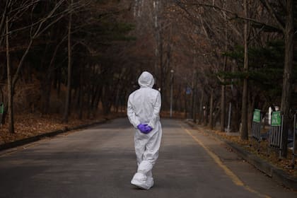 Un trabajador de la salud con traje protector camina por una calle desierta en Corea del Sur