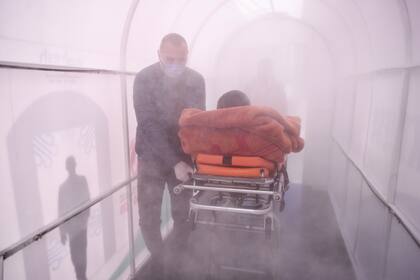 Un trabajador de salud lleva a un paciente a través de una cámara de desinfección configurada como medida preventiva en medio de las preocupaciones sobre la propagación de la Covid-19 frente a un hospital en Mitrovica el 7 de abril de 2020