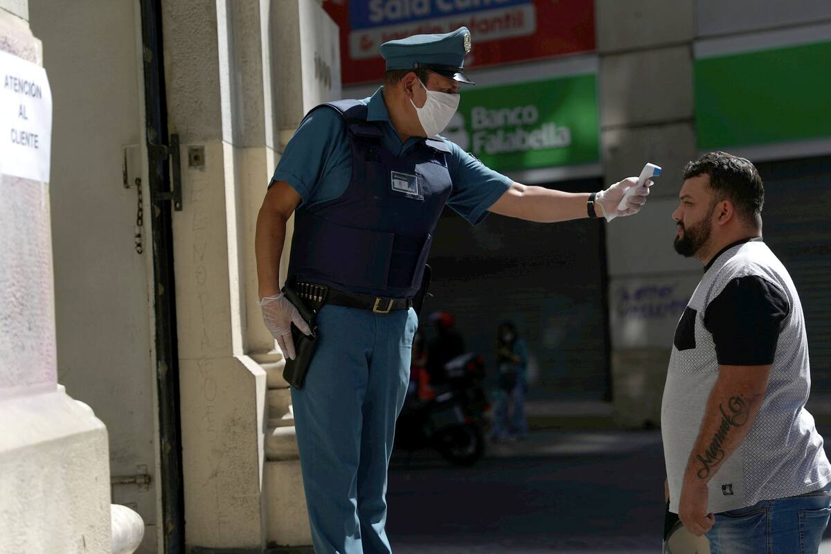 Un trabajador de seguridad bancaria verifica la temperatura de una persona en la calle frente a una sucursal bancaria, luego del brote de la enfermedad por coronavirus (COVID-19) en Santiago, Chile