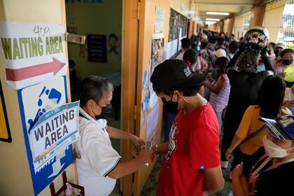Un trabajador electoral verifica la temperatura de un votante antes de que sufrague el lunes 9 de mayo de 2022 en un centro de votación en la ciudad de Quezón, Filipinas. (AP Foto/Aaron Favila)