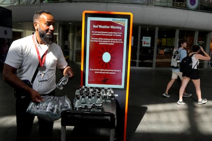 Un trabajador ferroviario reparte botellas de agua a los pasajeros en la estación ferroviaria de King's Cross
