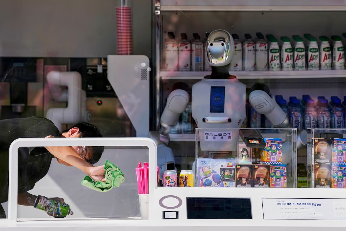 Un trabajador limpia el panel de una ventana junto a un robot humanoide compacto en un puesto de bebidas de un parque en Pekín, el miércoles 9 de septiembre de 2026. (Foto AP/Andy Wong)