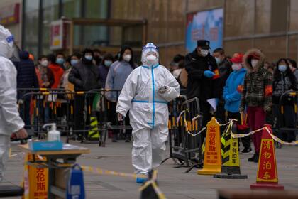 Un trabajador sanitario con vestimenta protectora pasa frente a vecinos que esperan en fila para recibir el test del coronavirus tras la detección de un caso de COVID-19 en un edificio residencial, miércoles 6 de abril de 2022 en Beijing. (AP Foto/Andy Wong)