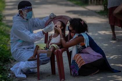 Un trabajador sanitario indio con traje de protección toma muestras nasales de una niña para una prueba de COVID-19 en el poblado de Burha Mayong, distrito de Morigaon, en Assam, India, el sábado 22 de mayo de 2021. (AP Foto/Anupam Nath)