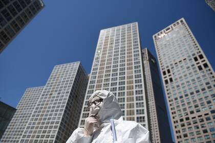 Un trabajador, vestido con un traje de protección en medio de las preocupaciones sobre el coronavirus, espera para verificar la temperatura de los conductores en la entrada del estacionamiento de un complejo comercial en Pekín el 22 de abril de 2020