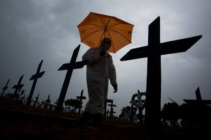 Un trabajador vestido con un traje protector y con un paraguas camina frente a las tumbas de las víctimas del Covid-19 en el cementerio de Nossa Senhora Aparecida, en Manaus