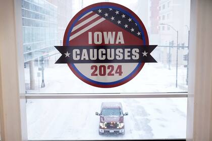 Un vehículo avanza en un camino nevado bajo una ventana con un cartel de las asambleas partidistas de Iowa el viernes 12 de enero de 2024 en el centro de Des Moines, Iowa