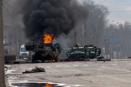 Un vehículo blindado de transporte de personal ruso arde en medio de vehículos utilitarios ligeros dañados y abandonados después de los combates en Kharkiv, Ucrania, el domingo 27 de febrero de 2022.