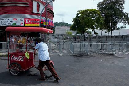 Un vendedor ambulante empuja su carro mientras una marcha de maestros avanza hacia la Plaza 5 de Mayo, cerca de unas barricadas de seguridad colocadas para bloquear el acceso a la Asamblea Nacional en Ciudad de Panamá, el jueves 14 de julio de 2022. (AP Foto/Arnulfo Franco)