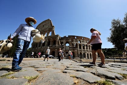 Un vendedor callejero con tapabocas ofrece sombreros de paja a los turistas fuera del monumento del Coliseo el 22 de agosto de 2020 en Roma durante la pandemia de coronavirus