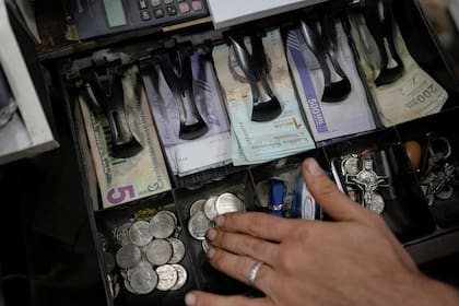 Un vendedor cuenta bolívares venezolanos y billetes de dólares estadounidenses para entregar cambio a un cliente en un mercado público en Caracas, Venezuela