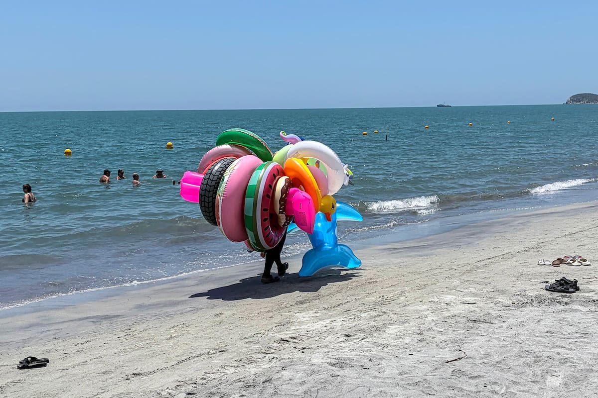 Un vendedor de flotadores inflables camina por la playa en Santa Marta, departamento de Magdalena, Colombia, el 19 de abril de 2026. A primera vista, parece una joya turística de postal, con aguas cristalinas del Caribe y montañas coronadas por picos nevados. Pero bajo la superficie de este idílico destino colombiano, la violencia paramilitar mantiene a comerciantes y comunidades indígenas viviendo con miedo. En la Sierra Nevada de Santa Marta, los turistas deambulan sin ser conscientes de la presencia de escuadrones camuflados que los vigilan de cerca, extorsionan a los negocios cercanos y siembran el terror entre las comunidades indígenas, cuyo conocimiento ancestral ha sido reconocido por la UNESCO como parte del patrimonio cultural mundial. (Foto de Luis ACOSTA / AFP)