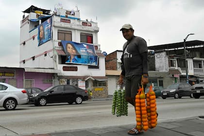 Un vendedor de frutas camino en una calle de Guayaquil, delante de carteles proselitistas de Luisa González. (Rodrigo BUENDIA / AFP)
