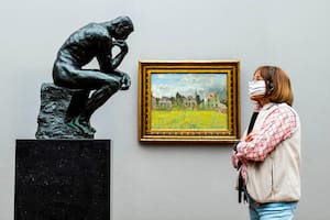Un visitante con una máscara facial mira la escultura icónica del escultor francés Auguste Rodin "The Thinker" en el museo Alte Nationalgalerie (Old National Gallery) en Berlín el 12 de mayo de 2020, después de que el museo reabrió sus puertas al público después de una relajación. de restr