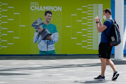 Un visitante se detiene para tomar una foto de una valla publicitaria con el campeón defensor,Novak Djokovic, antes del Abierto de Australia