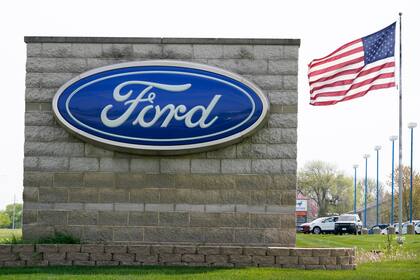 Una bandera estadounidense ondea junto a una concesionaria Ford, 27 de abril de 2021, en Waukee, Iowa. Ford dice que empezará a enviar por internet actualizaciones de su informática a algunos de sus modelos más nuevos, al ofrecer tecnología para igualar al fabricante de autos eléctricos Tesla. (AP Foto/Charlie Neibergall)