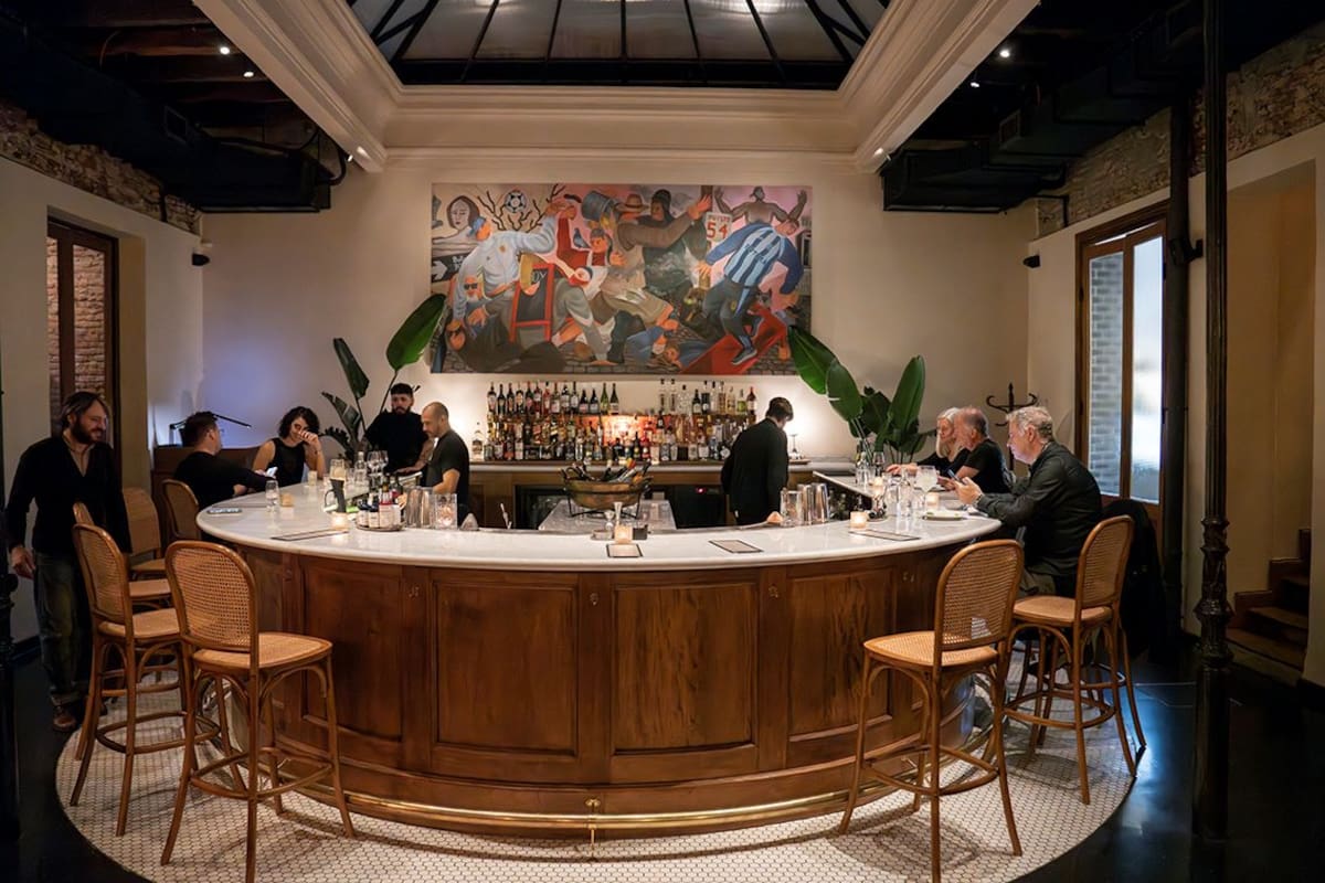 Una barra en mármol de carrara y forma de herradura, enmarcada por una obra del artista Martín Kazanietz, recibe y ordena el espacio.