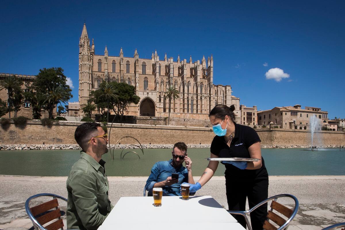 Una camarera con una máscara y guantes atiende a los clientes en un bar con terraza cerca de la Catedral de Palma de Mallorca el 11 de mayo de 2020, mientras España avanzaba para aliviar su estricto cierre por el coronavirus en ciertas regiones