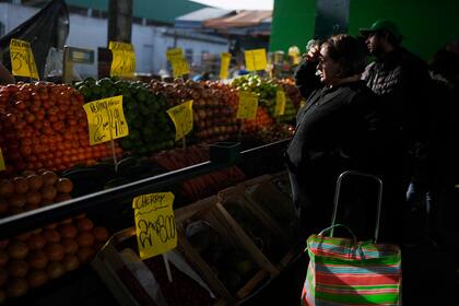 Una compradora cubre sus ojos ante los rayos de sol para revisar los precios expuestos de las frutas, en Buenos Aires