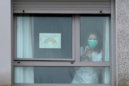 Una enfermera mira desde una ventana al lado de una pancarta que dice "Todo va a estar bien"