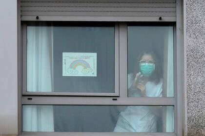 Una enfermera mira desde una ventana al lado de una pancarta que dice "Todo va a estar bien" dentro de un hogar de ancianos donde se encontraron cadáveres en los hogares de ancianos de Usera en Madrid, España, el martes 24 de marzo de 2020.