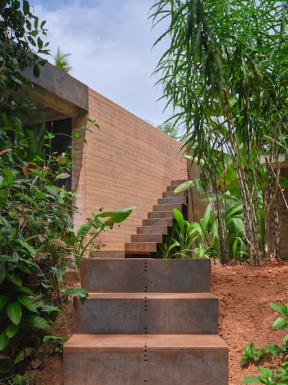 Una escalera de acero desciende siguiendo la pendiente natural y lleva hasta el agua, donde la casa se abre a la selva y al horizonte.