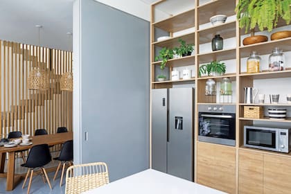 Una estantería de piso a techo en melamina maciza revestida en madera de roble miel (Ideï Arquitectura) aloja la heladera (Peabody), el horno (Domec Argentina) y el microondas (Sanyo).
