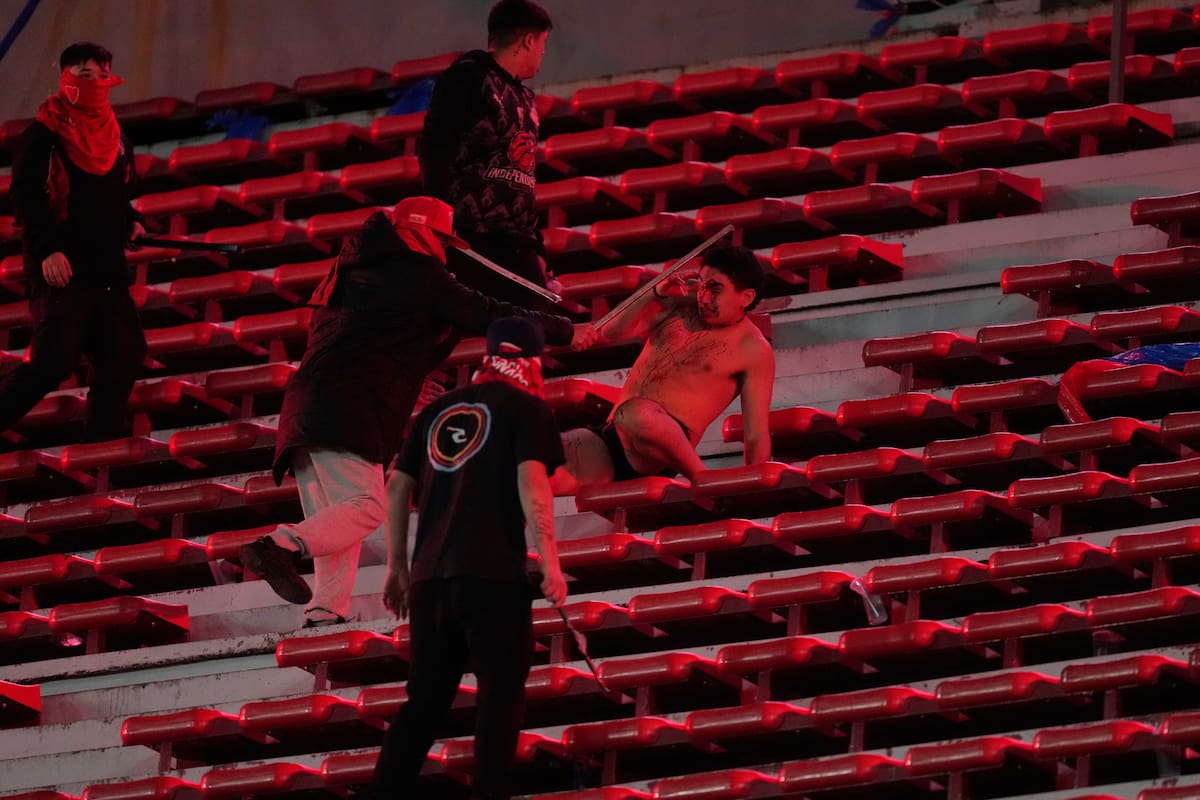 Una fanático de la Universidad de Chile (centro) es agredido por hinchas de Independiente de Argentina durante el partido por los octavos de final de la Copa Sudamericana, el miércoles 20 de agosto de 2025, en Avellaneda, Argentina. (AP Foto/Gustavo Garello)