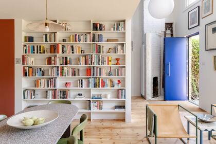 Una gran biblioteca empotrada en color blanco conecta los ambientes del living y la cocina comedor. Las sillas de la sala de estar están hechas de estructuras de acero tubular con revestimiento en polvo y asientos de cuero colgantes.