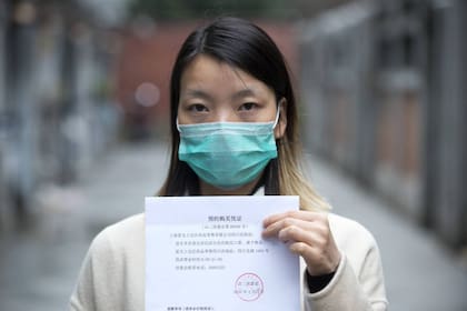 Una joven de Shanghái muestra la autorización oficial para adquirir las cinco mascarillas que el Gobierno ha destinado a cada familia