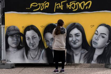 Una joven se para delante de un mural de las soldados retenidas por Hamás en Gaza, en Tel Aviv, Israel, el 17 de enero de 2025. La frase, en hebreo, dice "Mírelas a los ojos". (AP Foto/Maya Alleruzzo)
