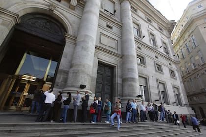 Una larga fila de personas espera ante las puertas de un banco oficial, en la ciudad de Buenos Aires