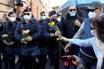 Una manifestante le da flores a un policía el viernes 15 de octubre de 2021 en el Circo Máximo de Roma, durante una protesta contra una nueva medida de combate al COVID-19 que requiere que todos los trabajadores presenten un pase de salud para poder ingresar a sus sitios laborales. (AP Foto/Gregorio Borgia)