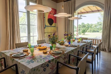 Una mesa larga domina el comedor, con grandes ventanales que dan al jardín. El mantel es de Milán: Nunzia compró un rollo de tela en un viaje a esa ciudad y, al volver a la Argentina, buscó a una costurera que se lo confeccionara al estilo italiano, que tiene pliegues especiales. “Para los que venimos de Milán, los detalles son importantes”. Las flores son de su jardín: “Me gusta la elegancia de lo simple”. La obra es de la artista Juliana Uriart.