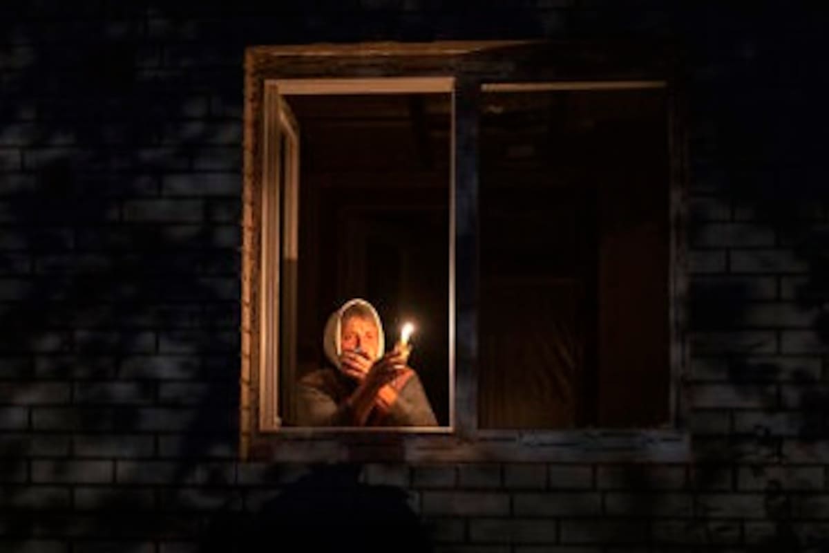 Una mujer alumbra con una vela desde su ventana ante los cortes de electricidad en Ucrania.
